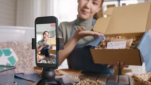 Female influecers showcasing a product in a cardboard box while filming herself on a smartphone.